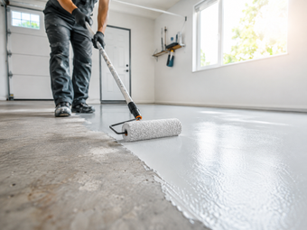 Professional installer applying a smooth gray epoxy coating to a concrete garage floor with a roller.