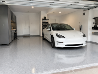 White electric sedan parked inside a clean residential garage with a glossy gray epoxy floor and built-in storage cabinets.