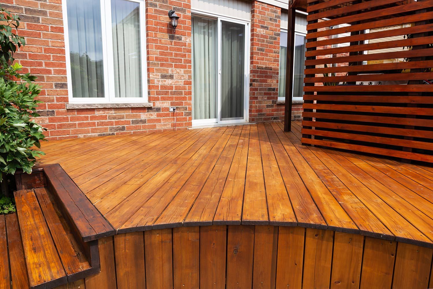 Curved wooden deck beside a brick house