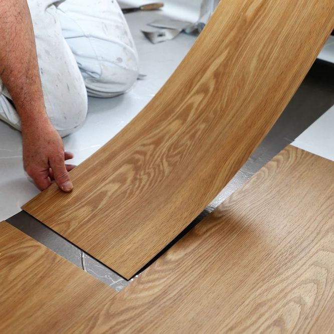 A person is laying a piece of wood on the floor.
