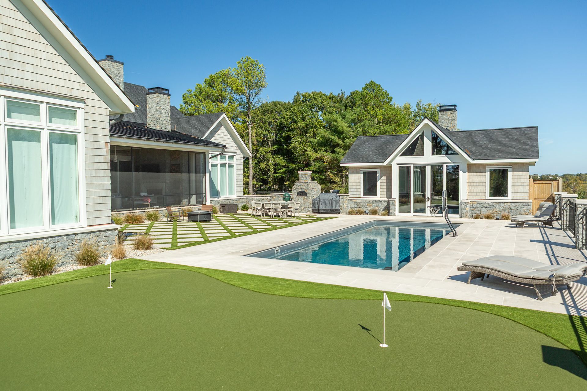 Backyard with pool, putting green, and a small guesthouse on a sunny day.