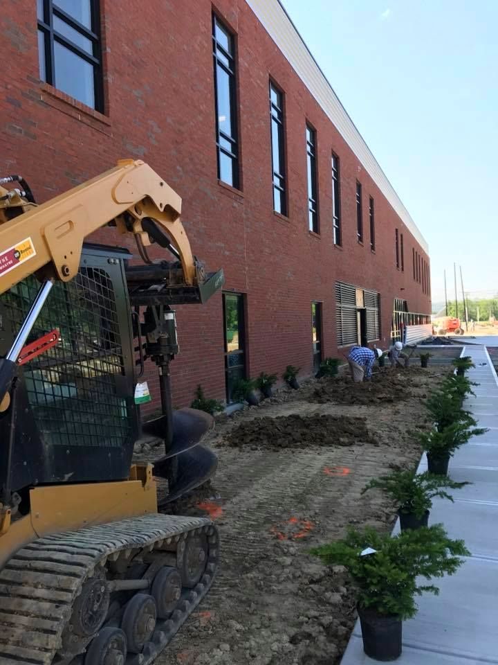 Construction outside a brick building; a skid steer and workers are planting landscaping.