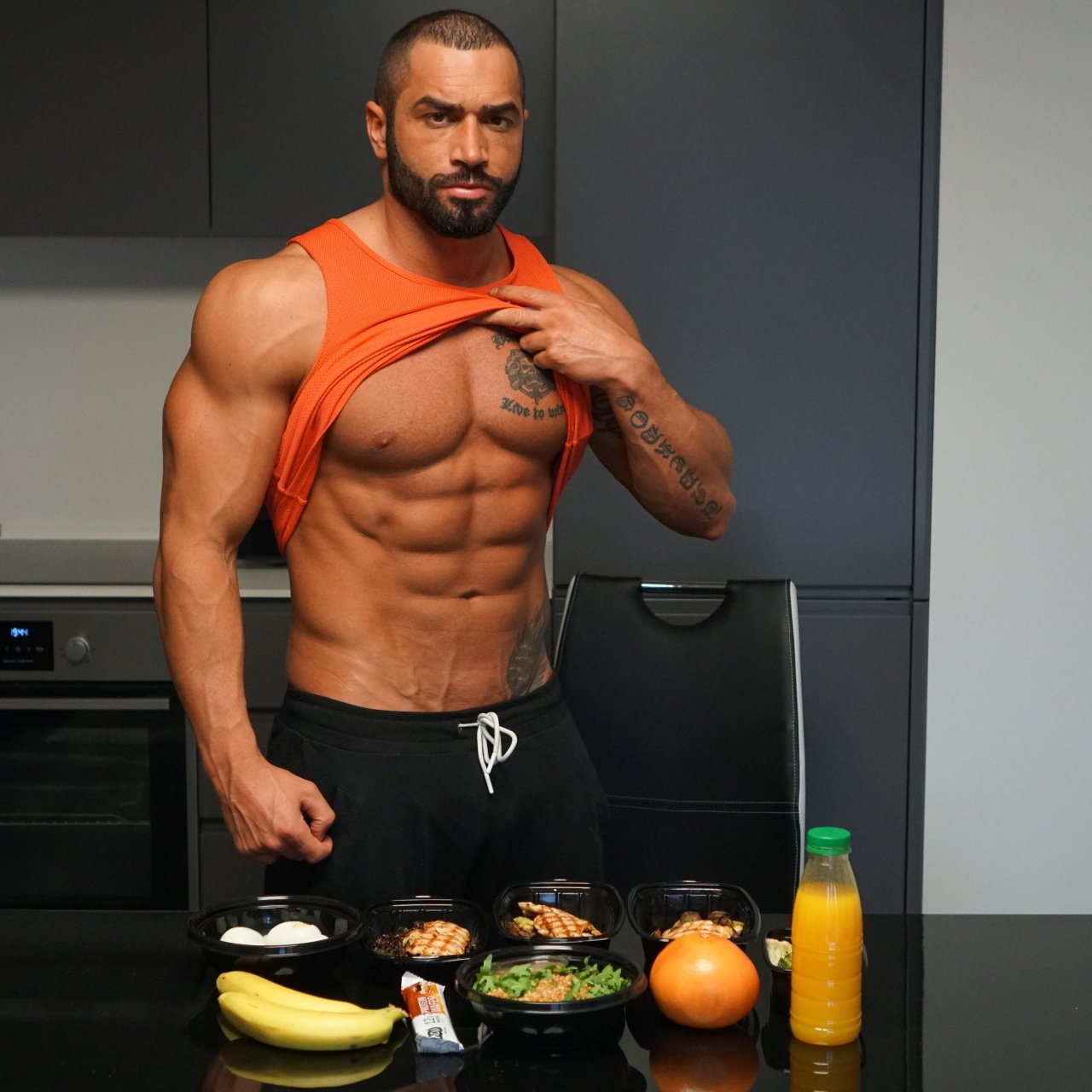 A shirtless man is standing in front of a table with bowls of food and a bottle of orange juice
