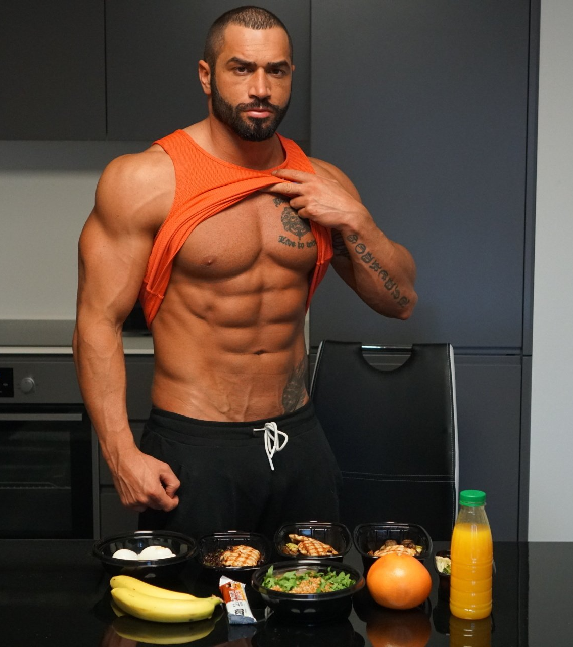 A shirtless man is standing in front of a table with bowls of food and a bottle of orange juice