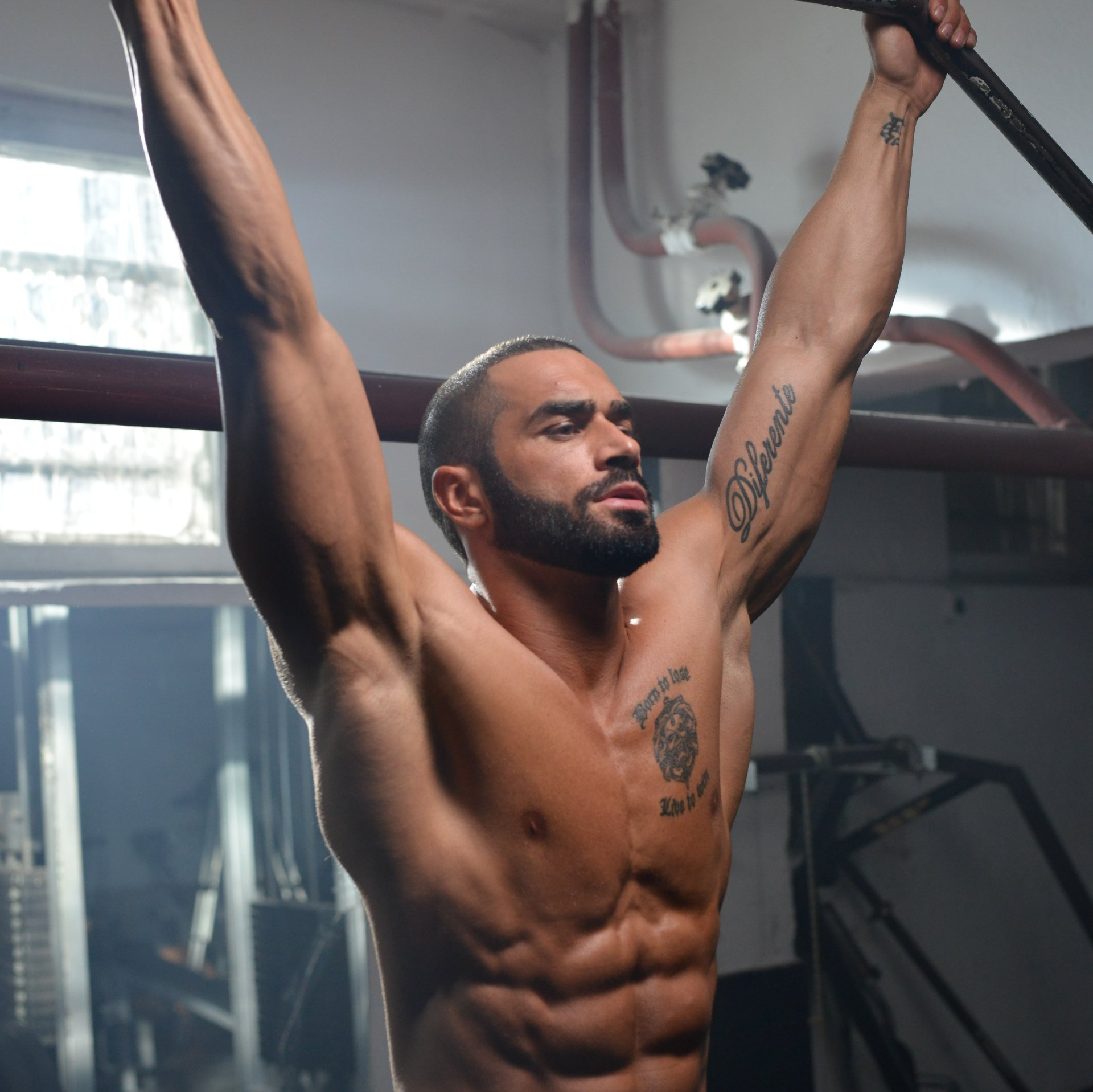 A shirtless man with a tattoo on his arm hanging from a bar