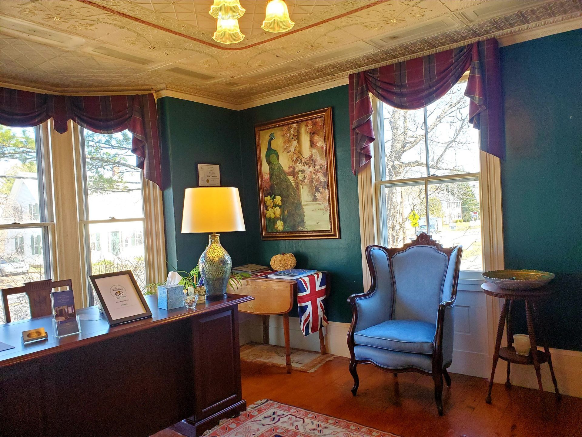 A living room with a desk , chair , lamp and a painting on the wall.