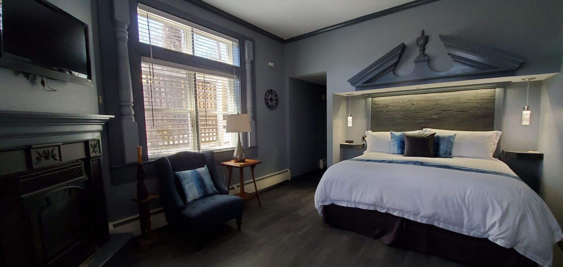 A bedroom with a king size bed , chair , television and fireplace.