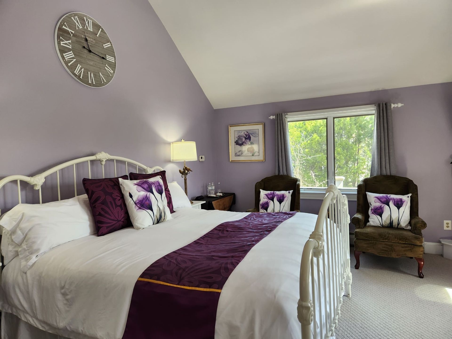 A bedroom with purple walls and a clock on the wall above the bed