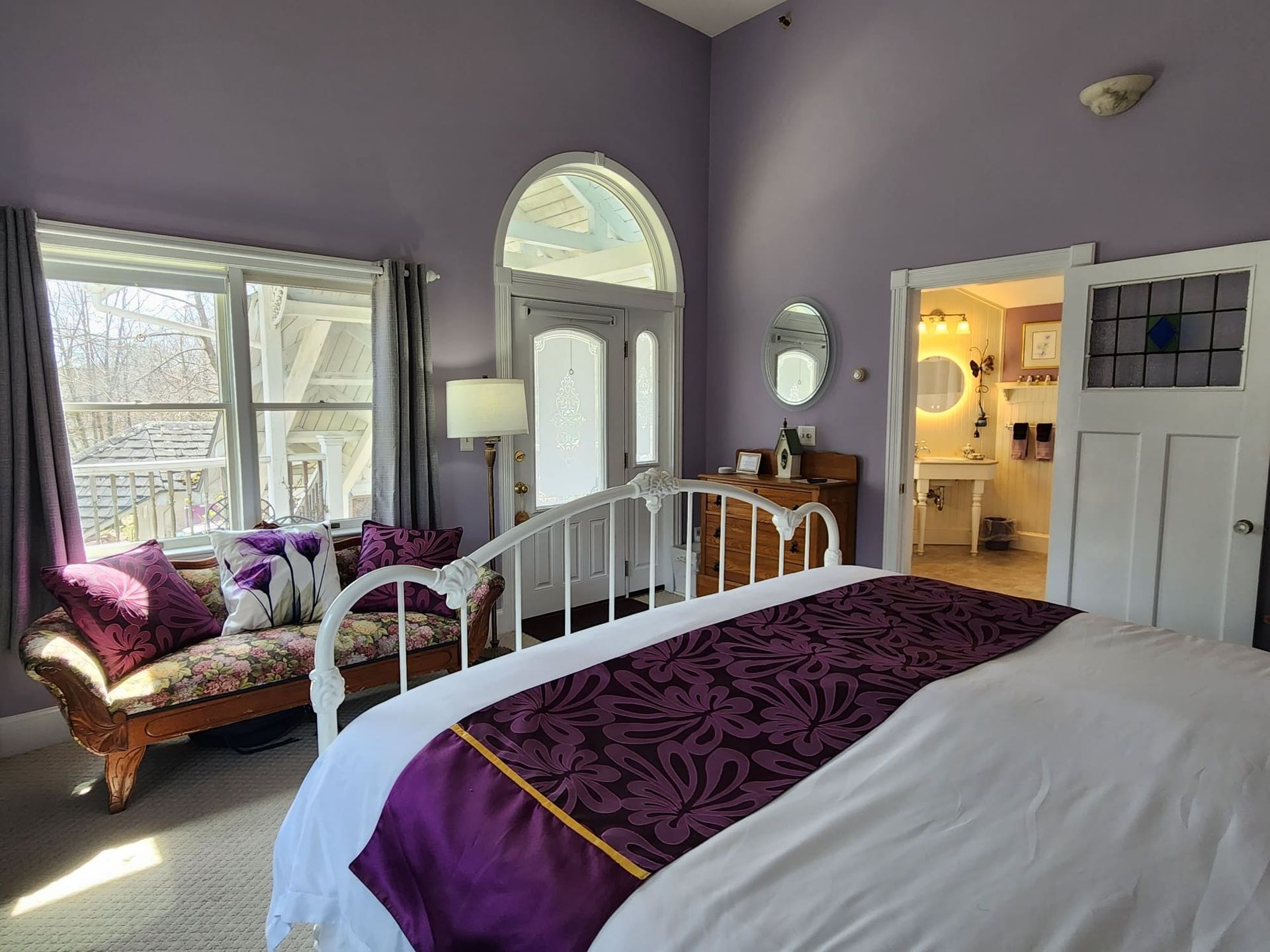 A bedroom with purple walls , a bed , a couch and a window.