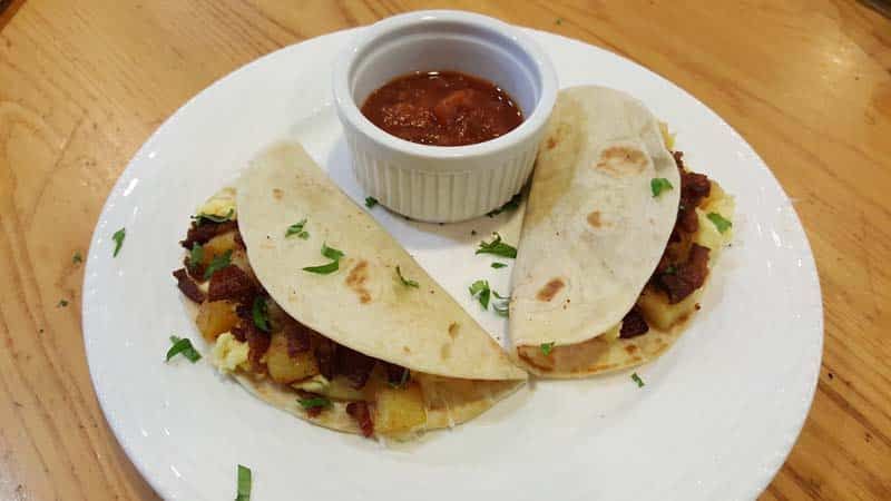 A white plate topped with two tacos and a bowl of salsa.