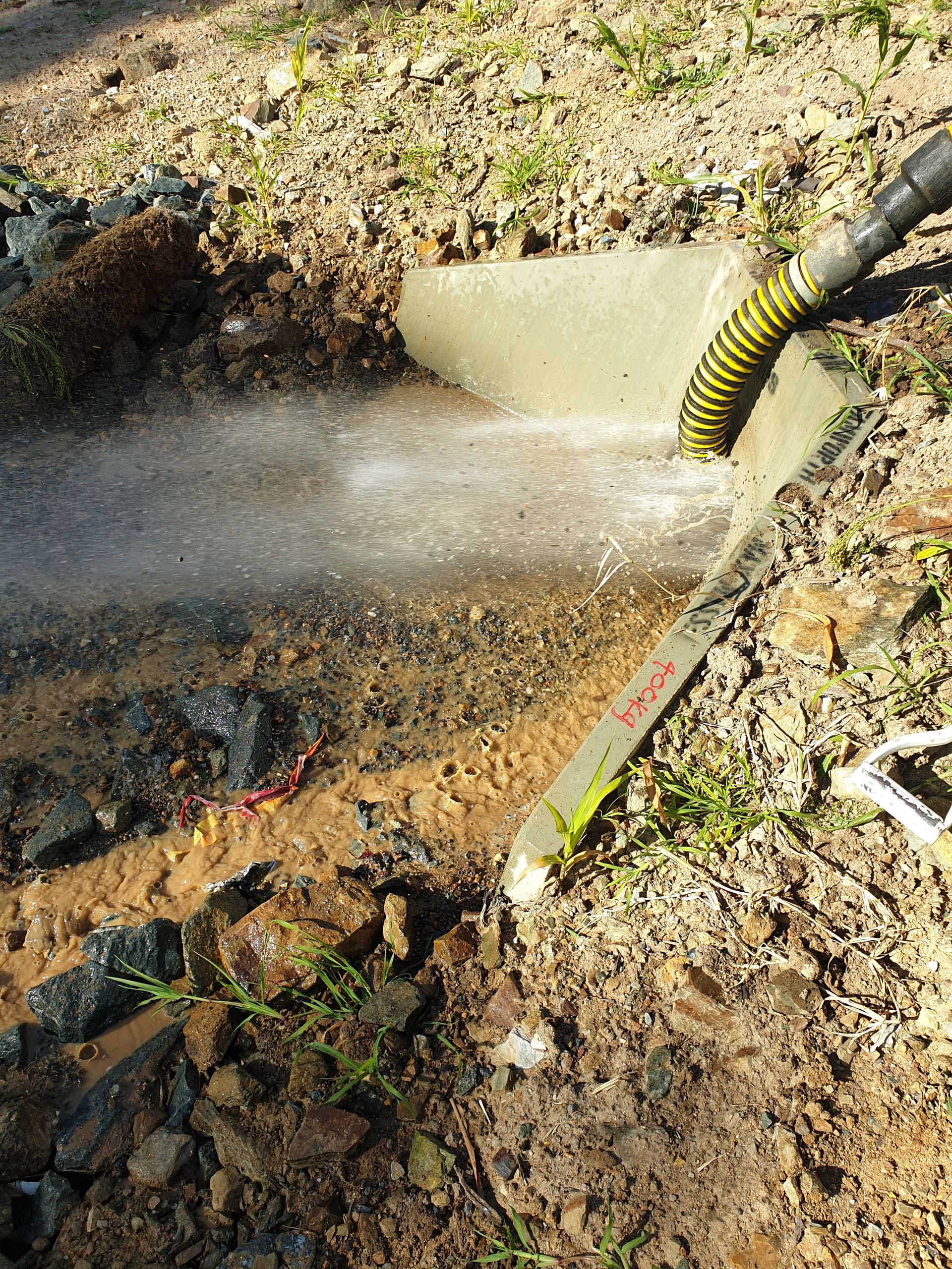 A hose spraying water into a hole in the dirt, creating a misty spray — Pro Pipe Solutions in Queanbeyan, NSW