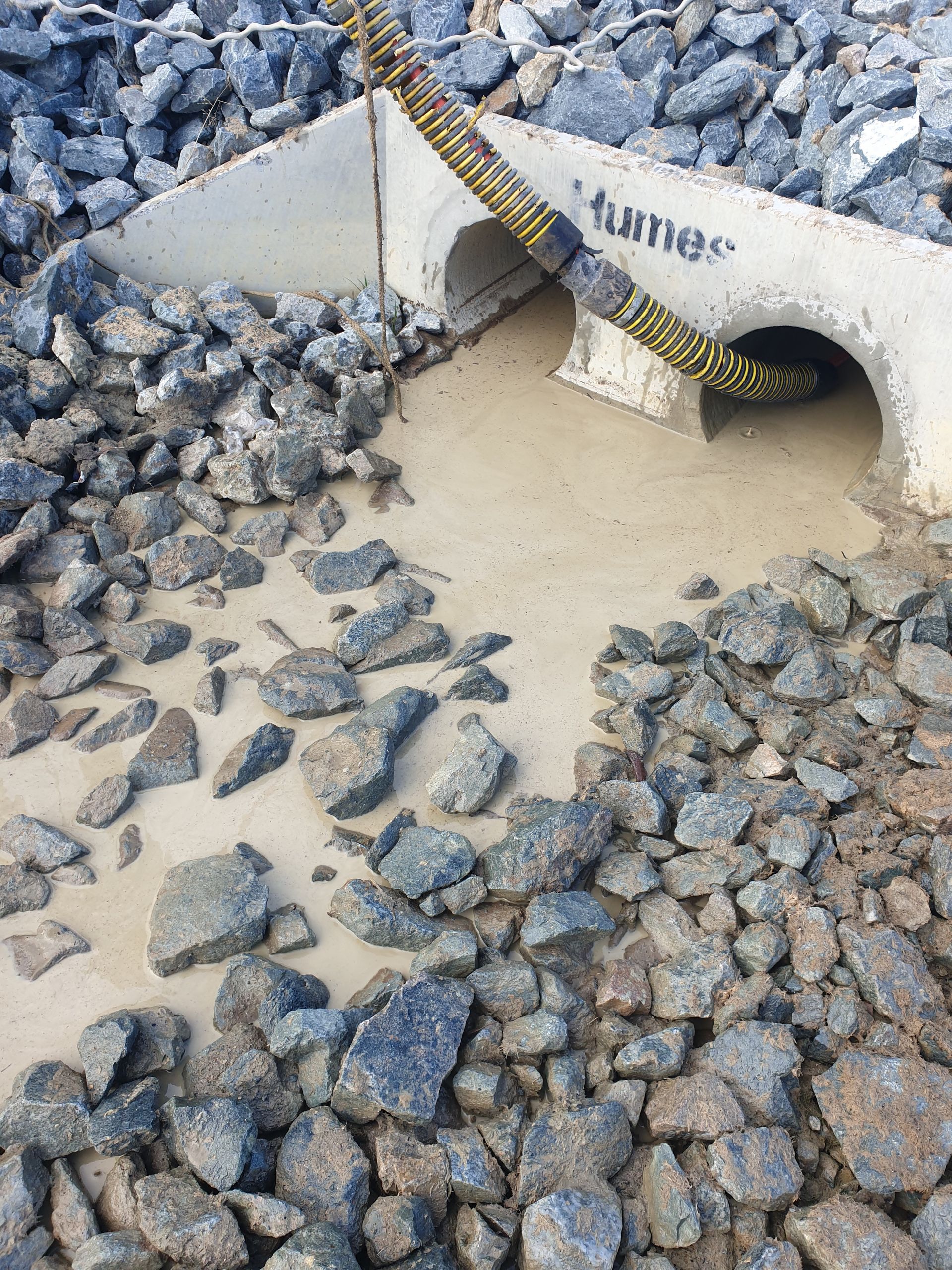 Concrete drain opening surrounded by rocks; yellow hose enters the opening — Pro Pipe Solutions in Queanbeyan, NSW