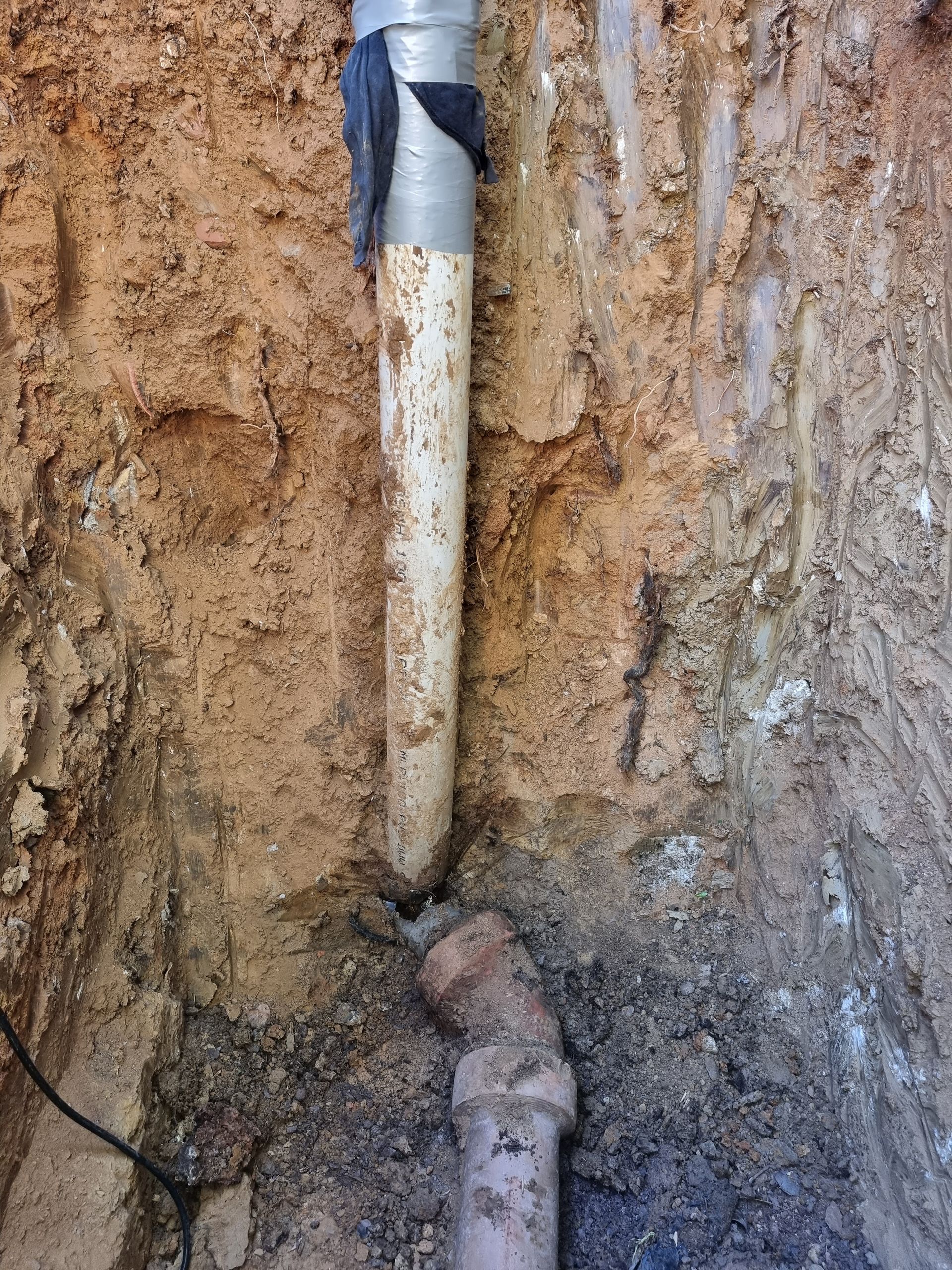 A vertical white pipe in a trench connects to a curved brown pipe. Soil surrounds the pipes — Pro Pipe Solutions in Queanbeyan, NSW