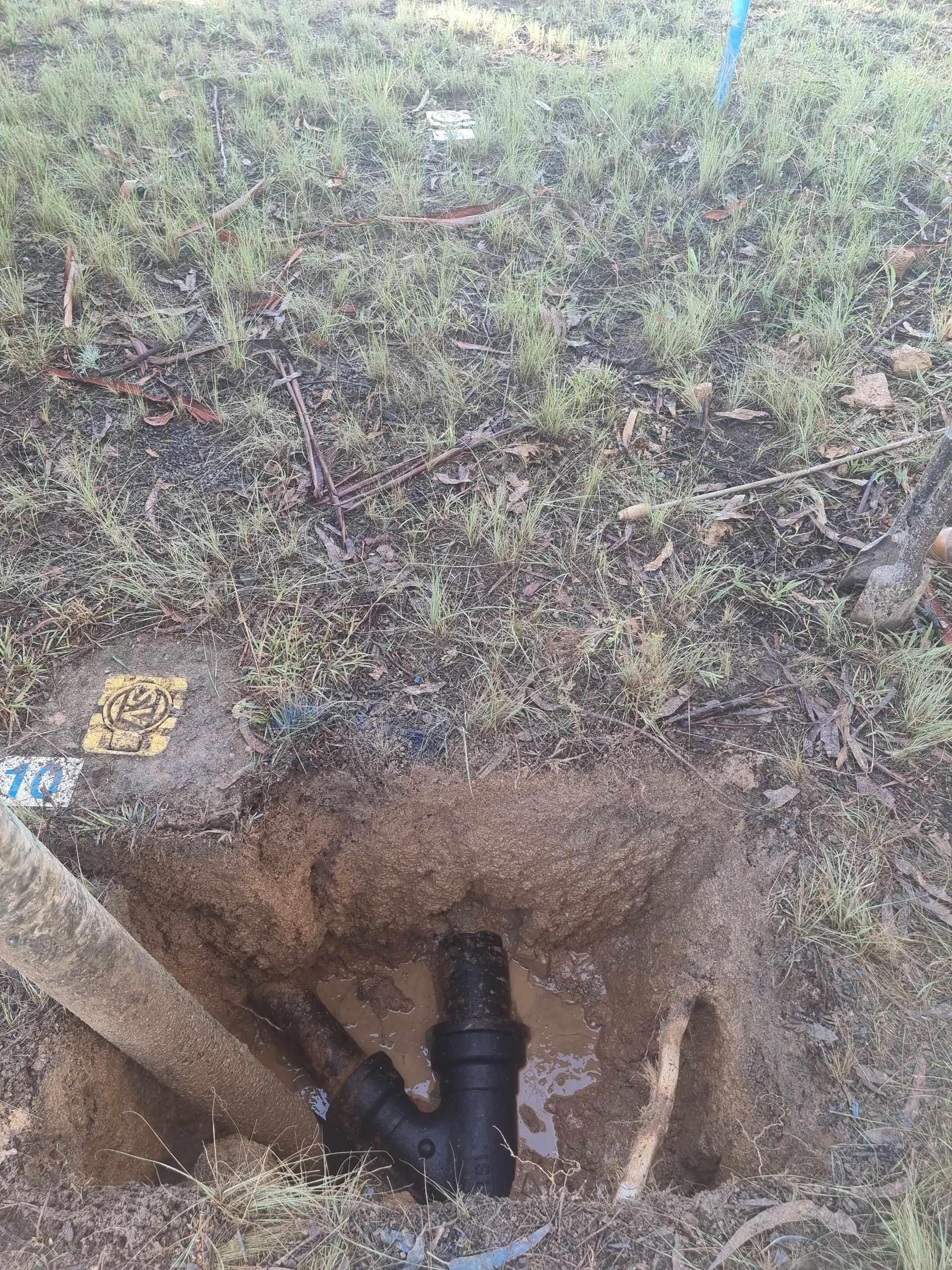Hole in the ground revealing black pipes, likely for water or sewage, surrounded by grass and dirt — Pro Pipe Solutions in Queanbeyan, NSW