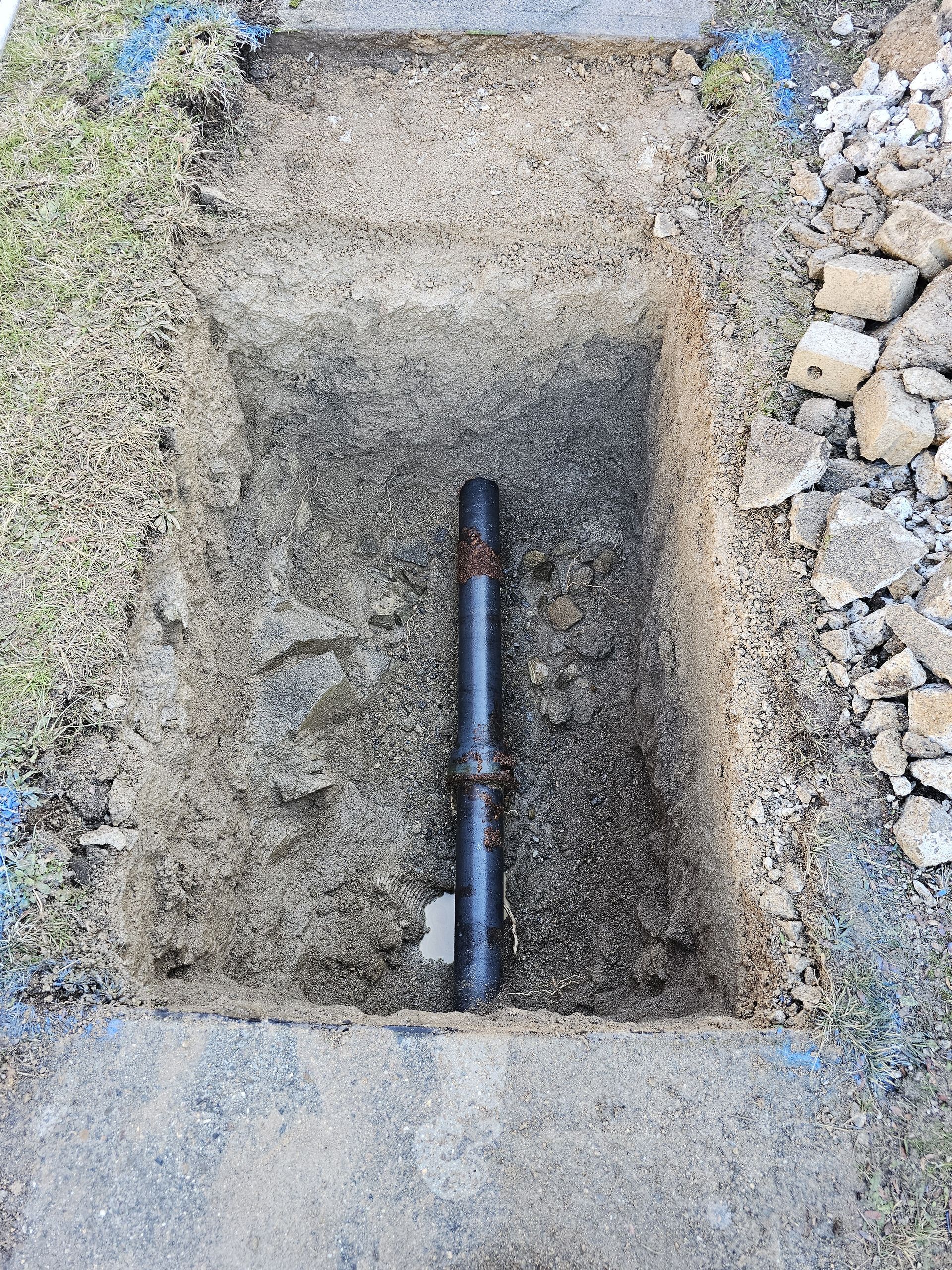 Black pipe section in a rectangular excavated area, surrounded by dirt and gravel — Pro Pipe Solutions in Queanbeyan, NSW