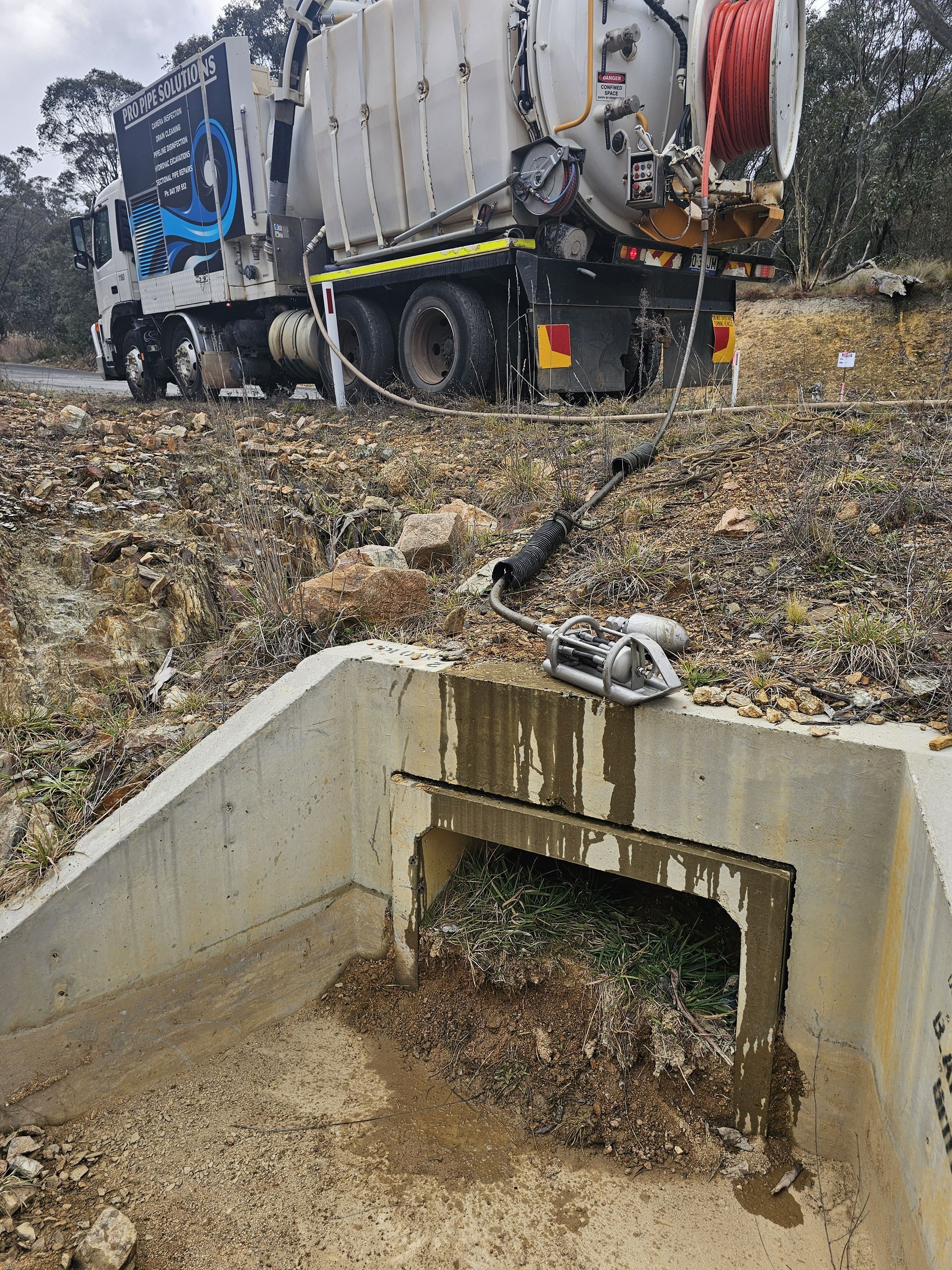 Truck cleaning debris from a concrete culvert, outdoors. Mud and green plant material visible — Pro Pipe Solutions in Queanbeyan, NSW