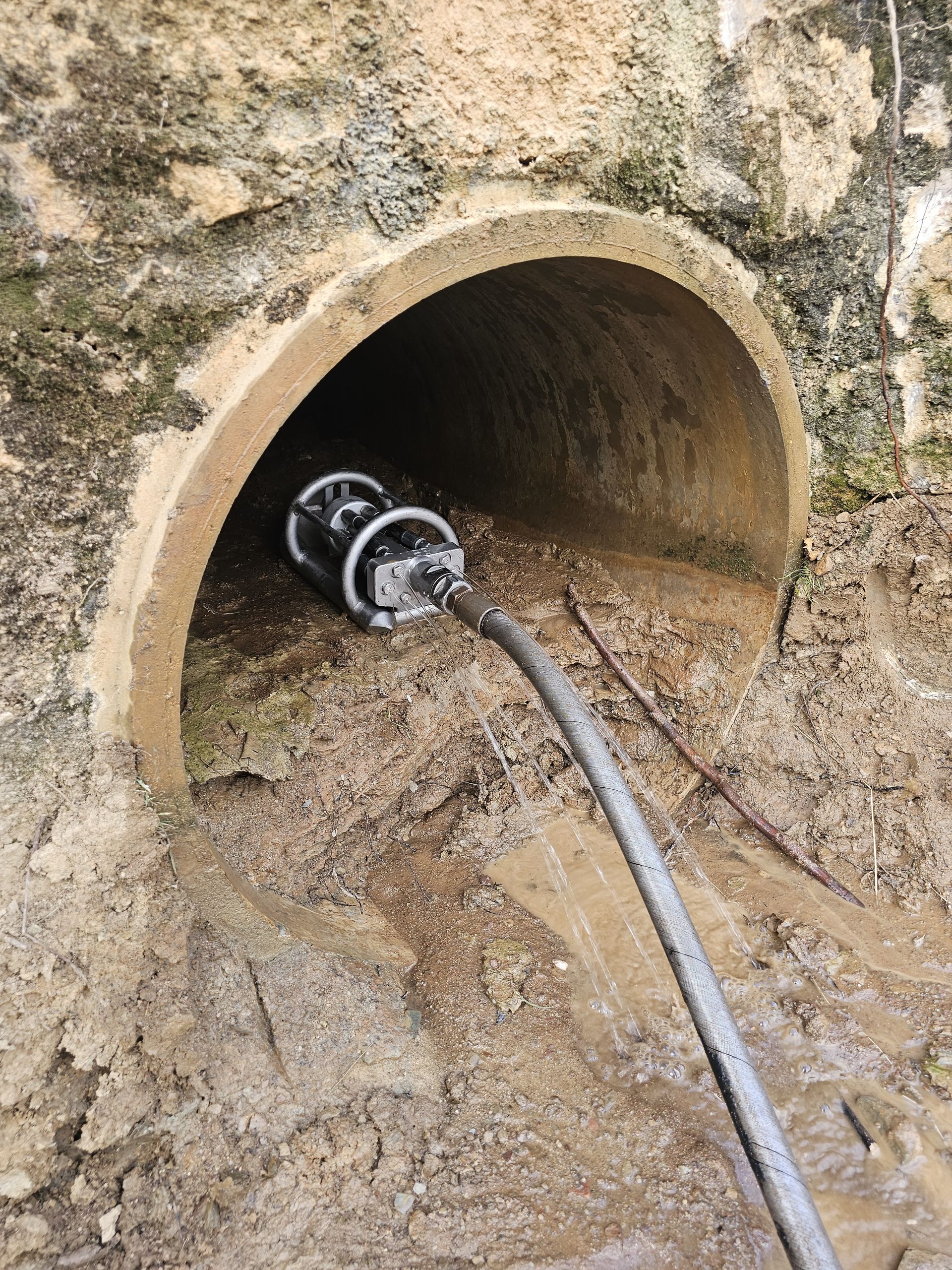 A camera on wheels inside a concrete pipe. A hose is attached, and the surrounding area is muddy — Pro Pipe Solutions in Braidwood, NSW
