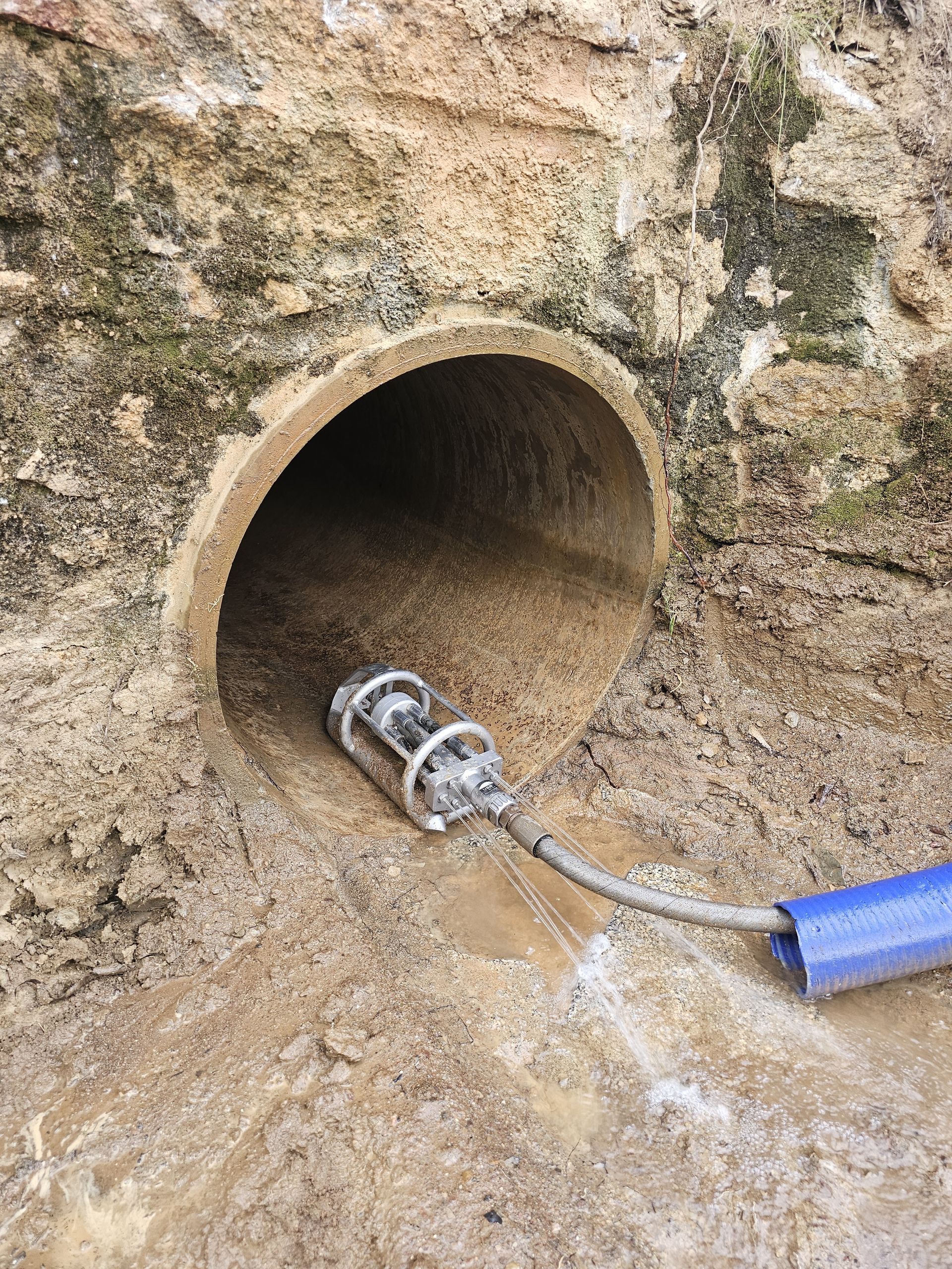 A cylindrical pipe opening in a weathered stone wall, with a camera and hose inserted — Pro Pipe Solutions in Queanbeyan, NSW