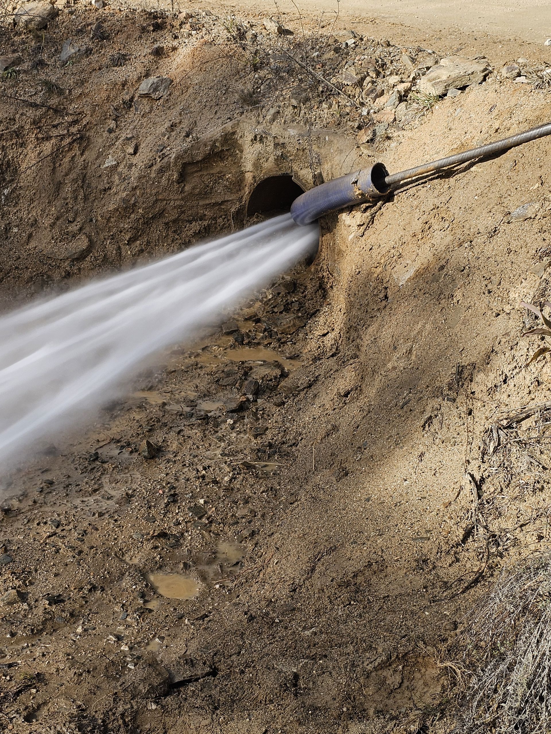 Water gushing forcefully from a pipe emerging from a hole in a dirt embankment — Pro Pipe Solutions in Queanbeyan, NSW