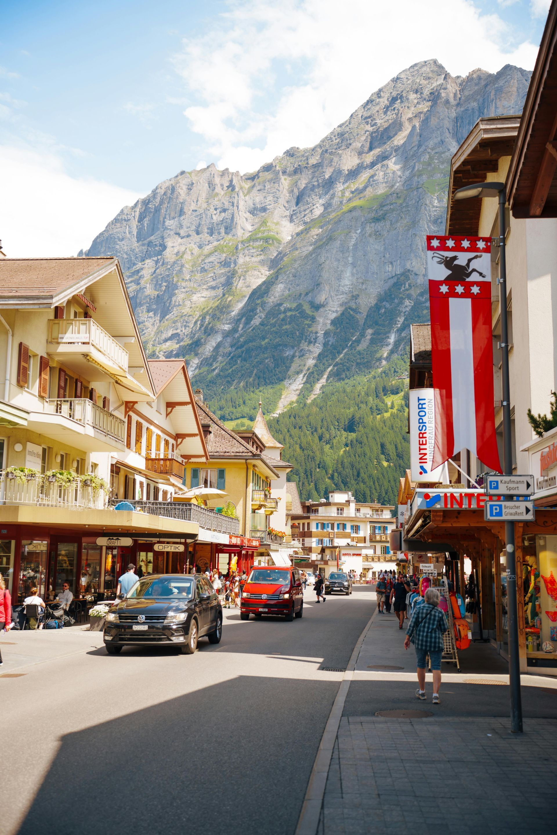 Busy mountain town street with cars, shops, and steep cliffs in the background