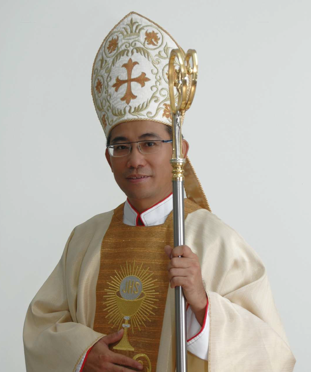 Bishop in ornate vestments, holding a crosier and wearing glasses.