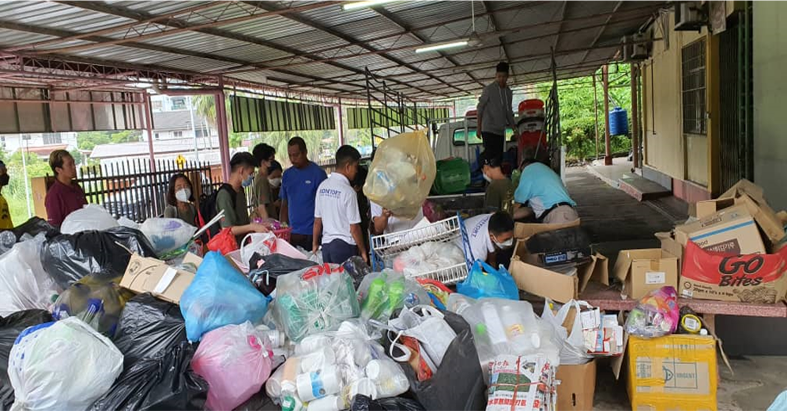 People sorting through piles of donations at an outdoor collection site, under a covered area.