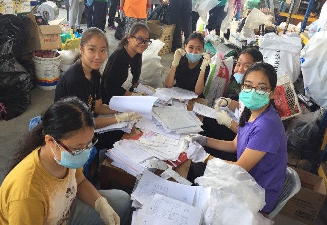 Group of people sorting papers, wearing masks and gloves, in a cluttered indoor setting.