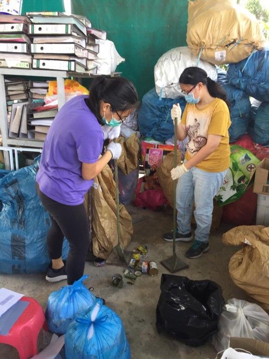 Two people wearing masks and gloves sorting through bags of recyclables.