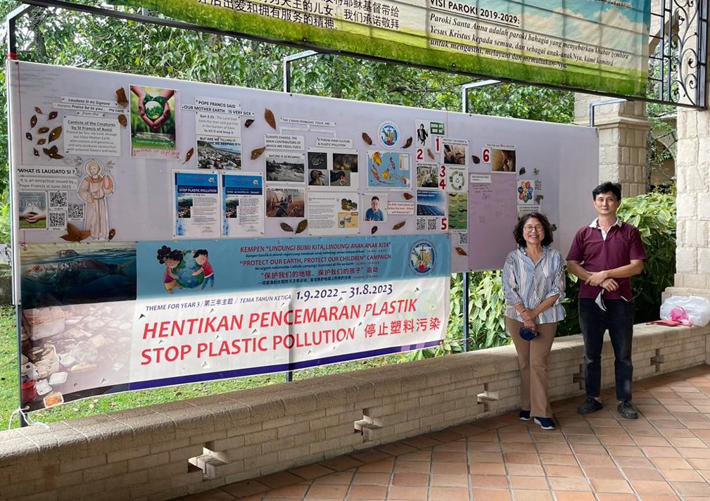 Two people stand by a poster about stopping plastic pollution.