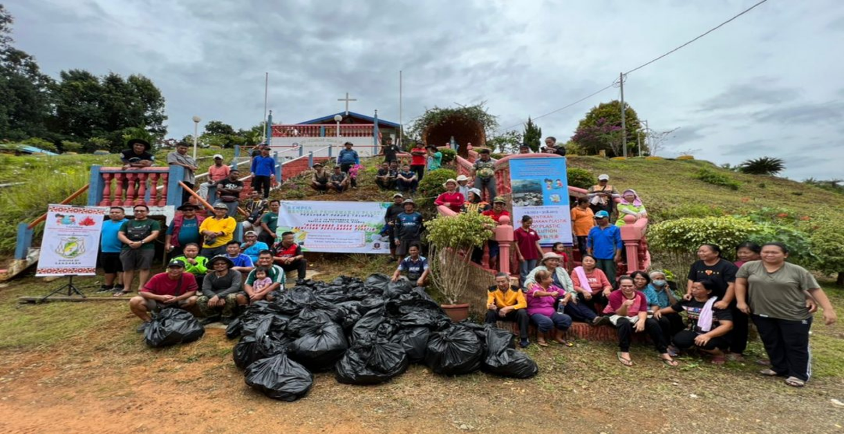 Group of people pose after a cleanup event; holding trash bags near sign promoting environmental awareness.