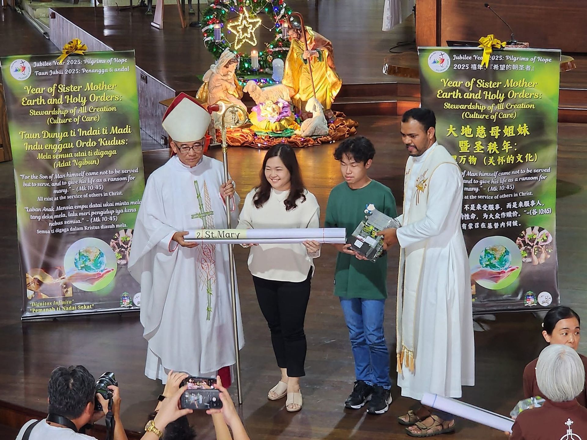 Church event: Two religious figures with two others hold items near a nativity scene.
