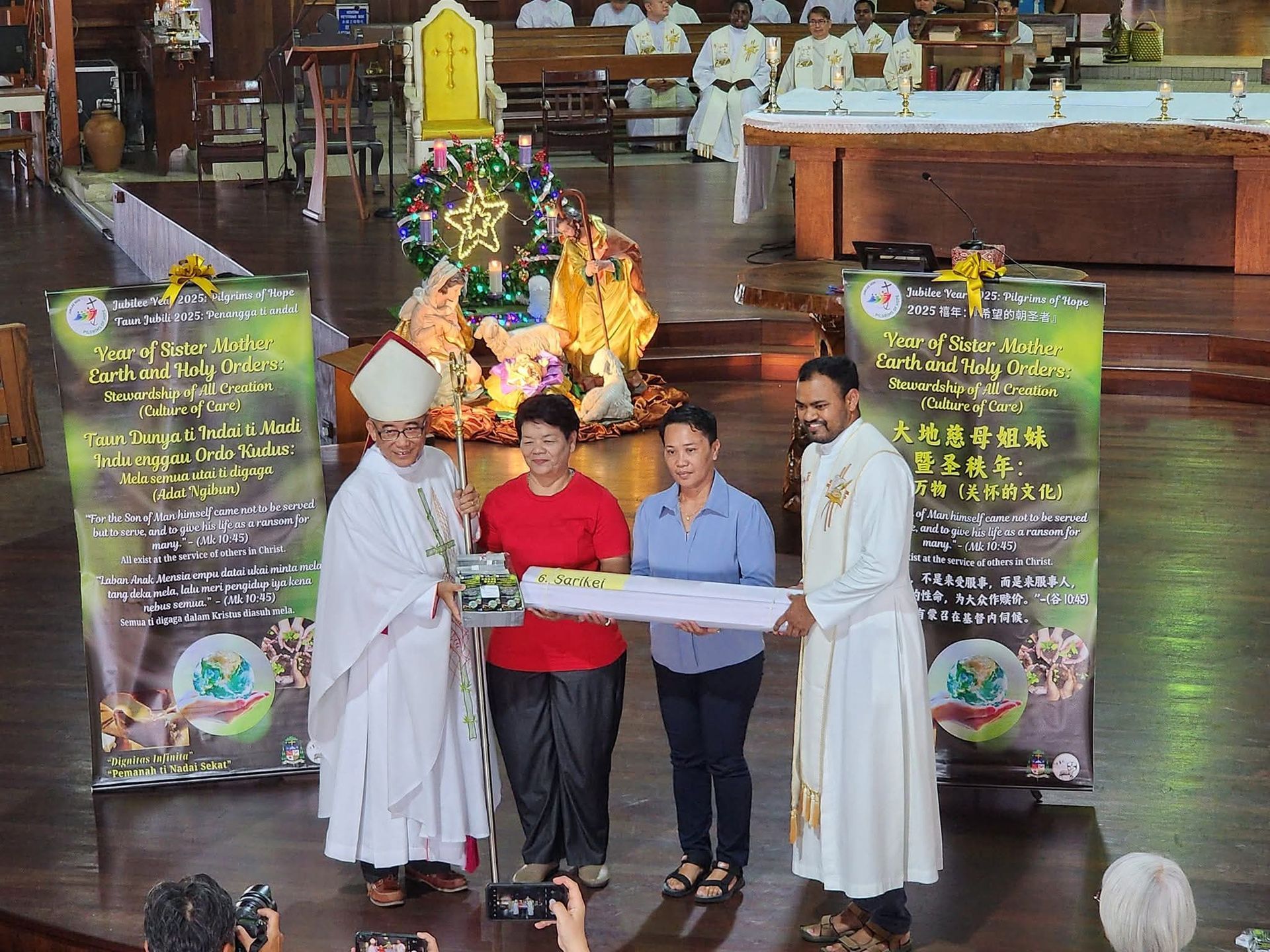 Clergy presenting gifts to two women on a stage in a church, decorated for Christmas.