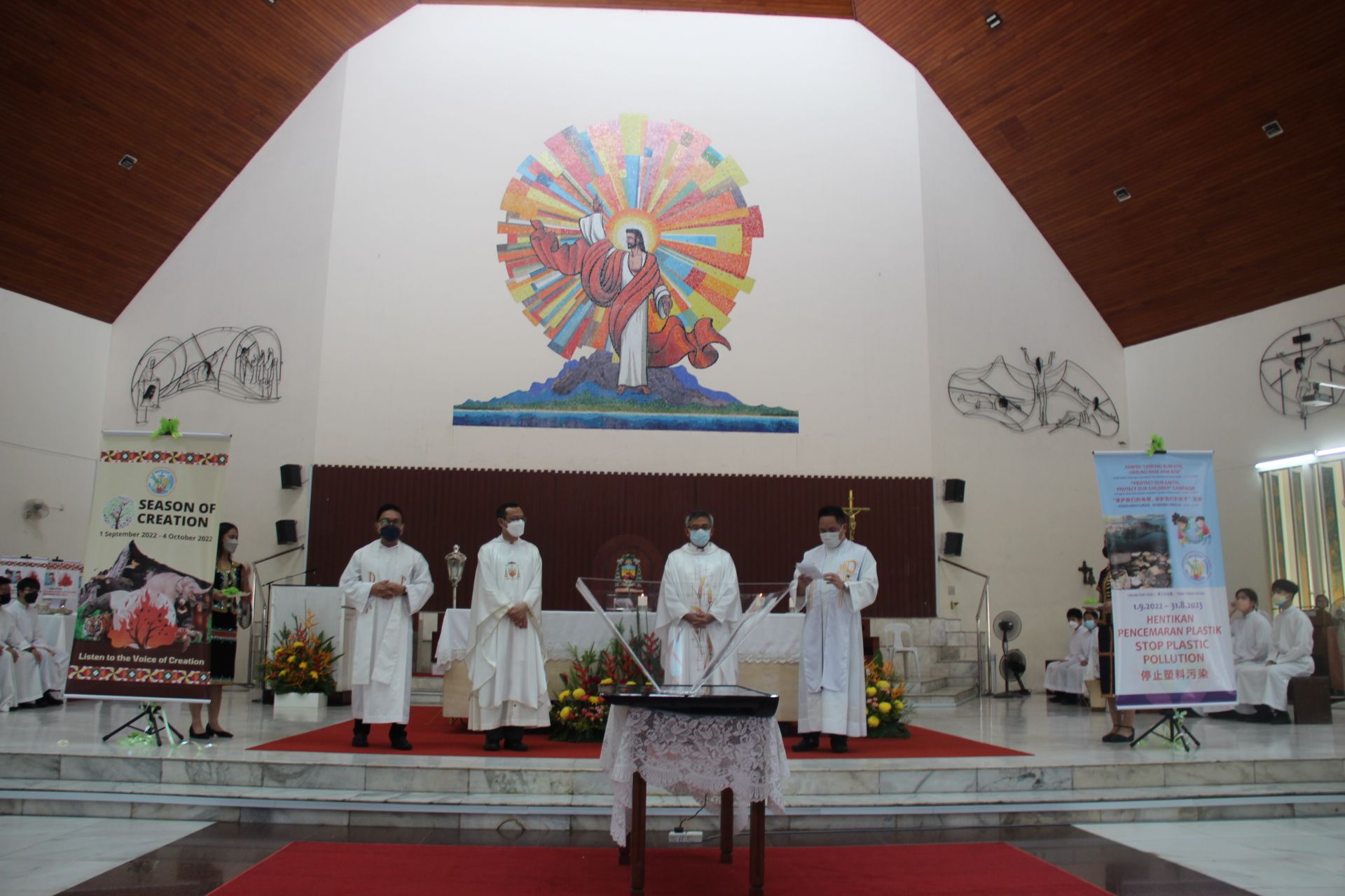 Clergy in white robes stand at an altar in a church. A large mosaic of Jesus is behind them.
