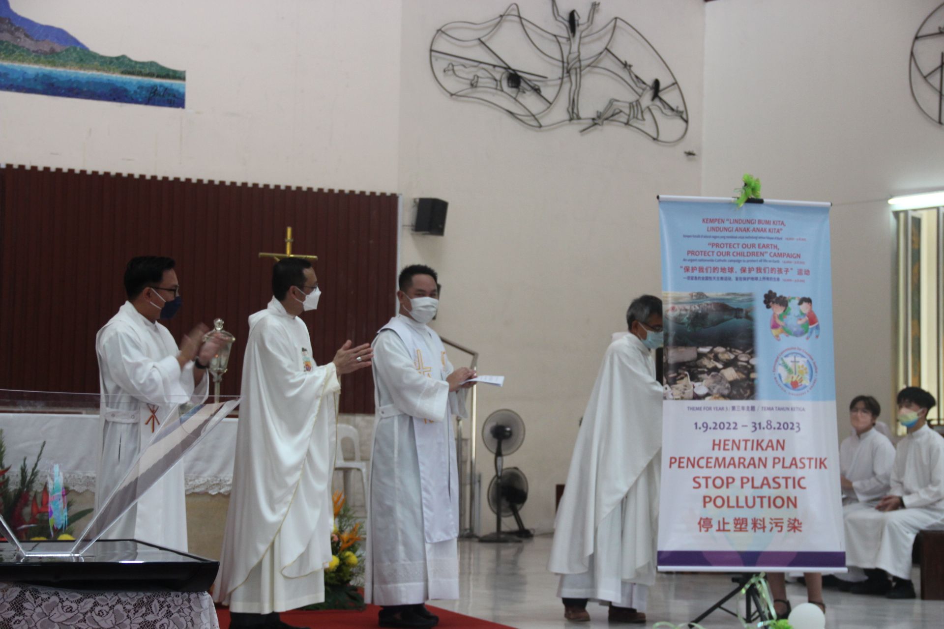 Clergy in white robes holding a sign about plastic pollution in a church setting.