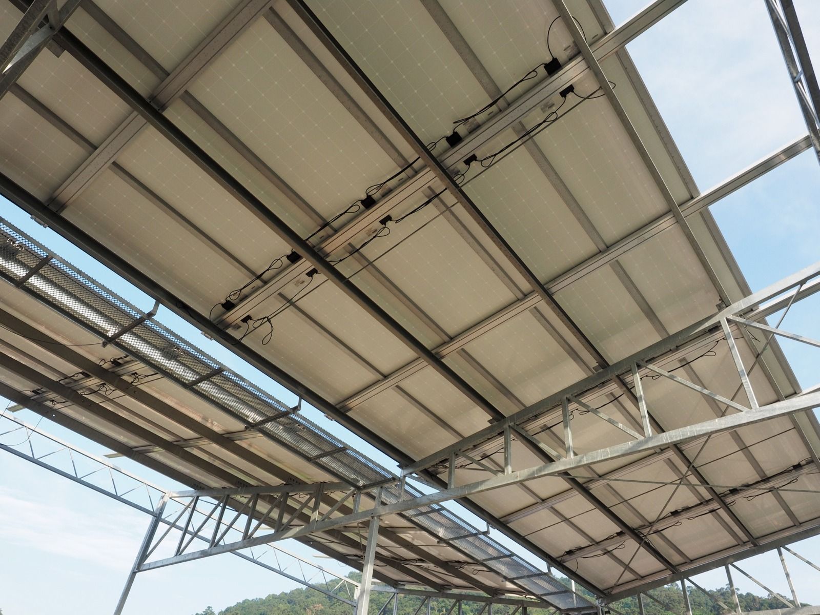 Underside of solar panels on a metal frame, against a blue sky, wires visible.