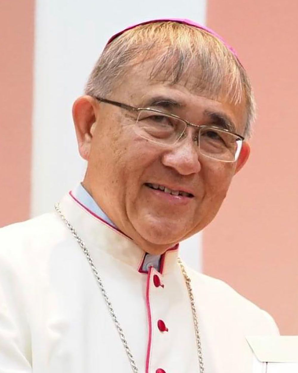 A man in ecclesiastical vestments, wearing glasses, smiling.