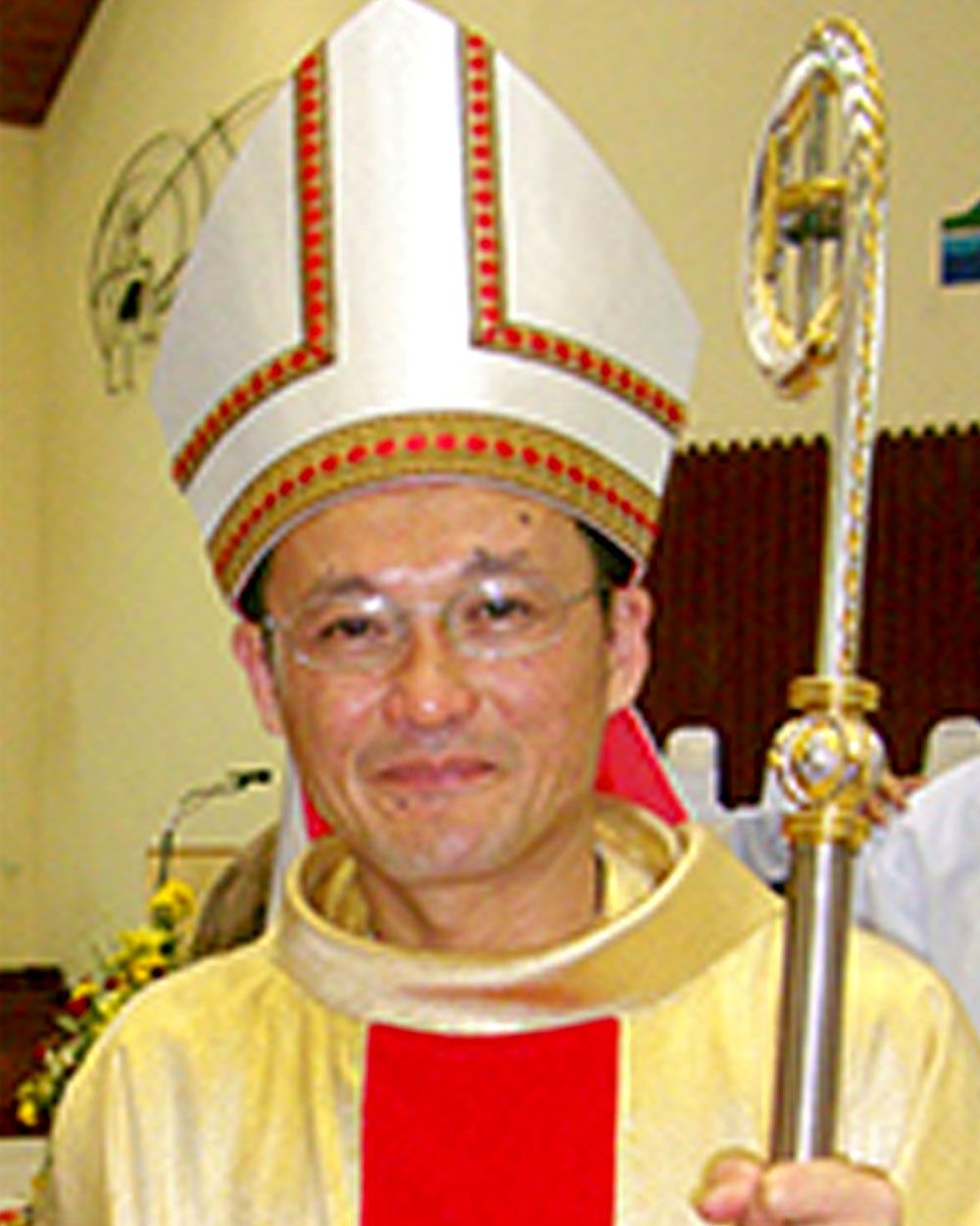 Bishop wearing mitre and vestments, holding a staff.