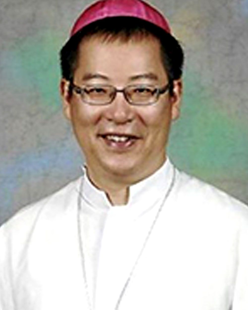 Clergyman wearing glasses, a white collar, and a magenta zucchetto, smiling.