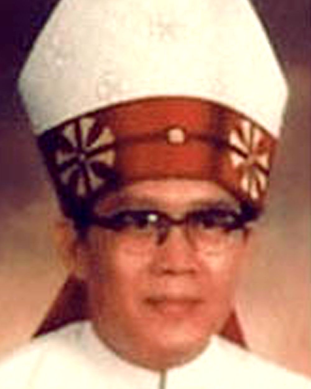 Man in glasses and mitre, wearing red and white ecclesiastical garb.