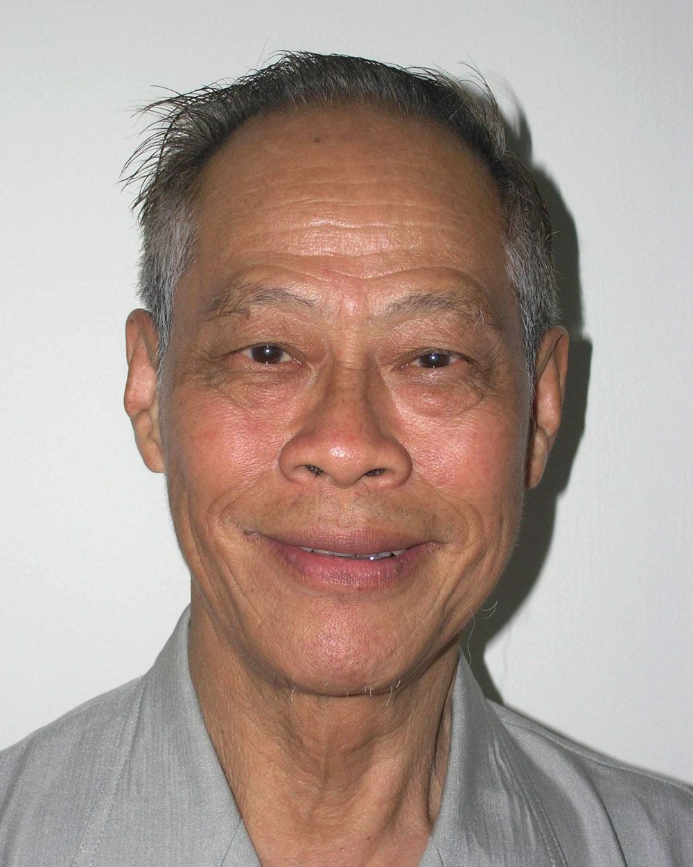 A smiling older person with short gray hair and brown eyes against a plain background.