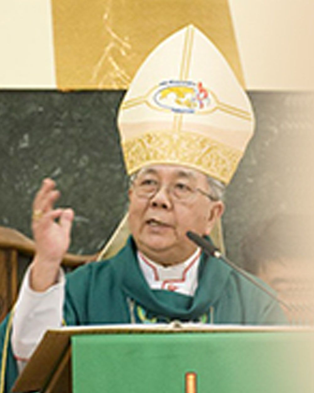 Clergyman speaking at a lectern, wearing a green robe and white mitre.