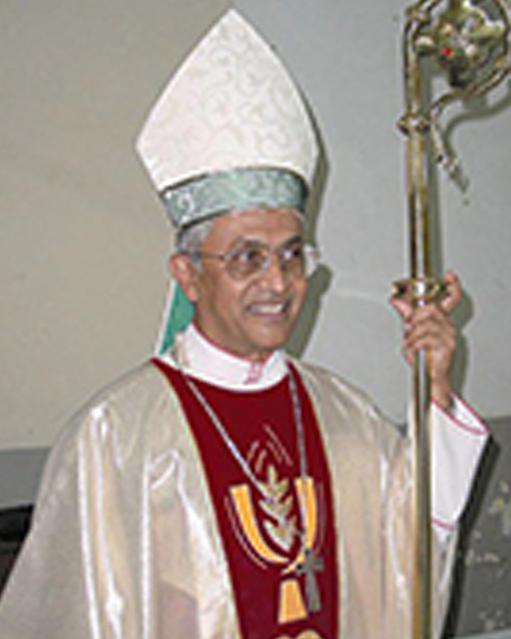 Bishop in white and maroon vestments, holding a staff, smiling.