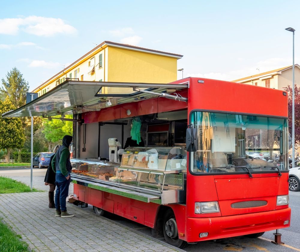 Red food truck with open serving window, customers are ordering.  Street setting.