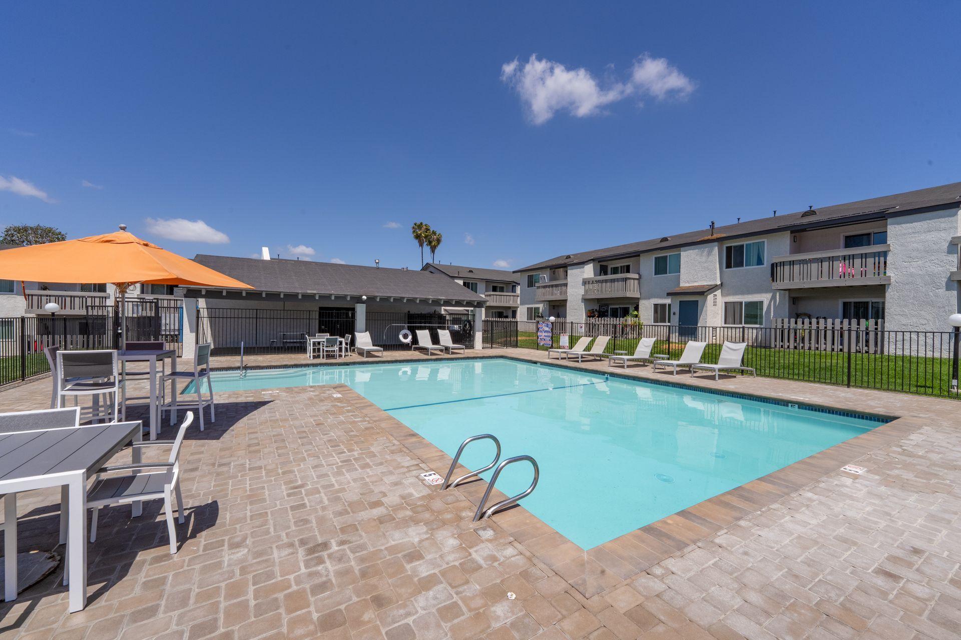 Apartment courtyard pool with lounge chairs and orange umbrellas under a blue sky