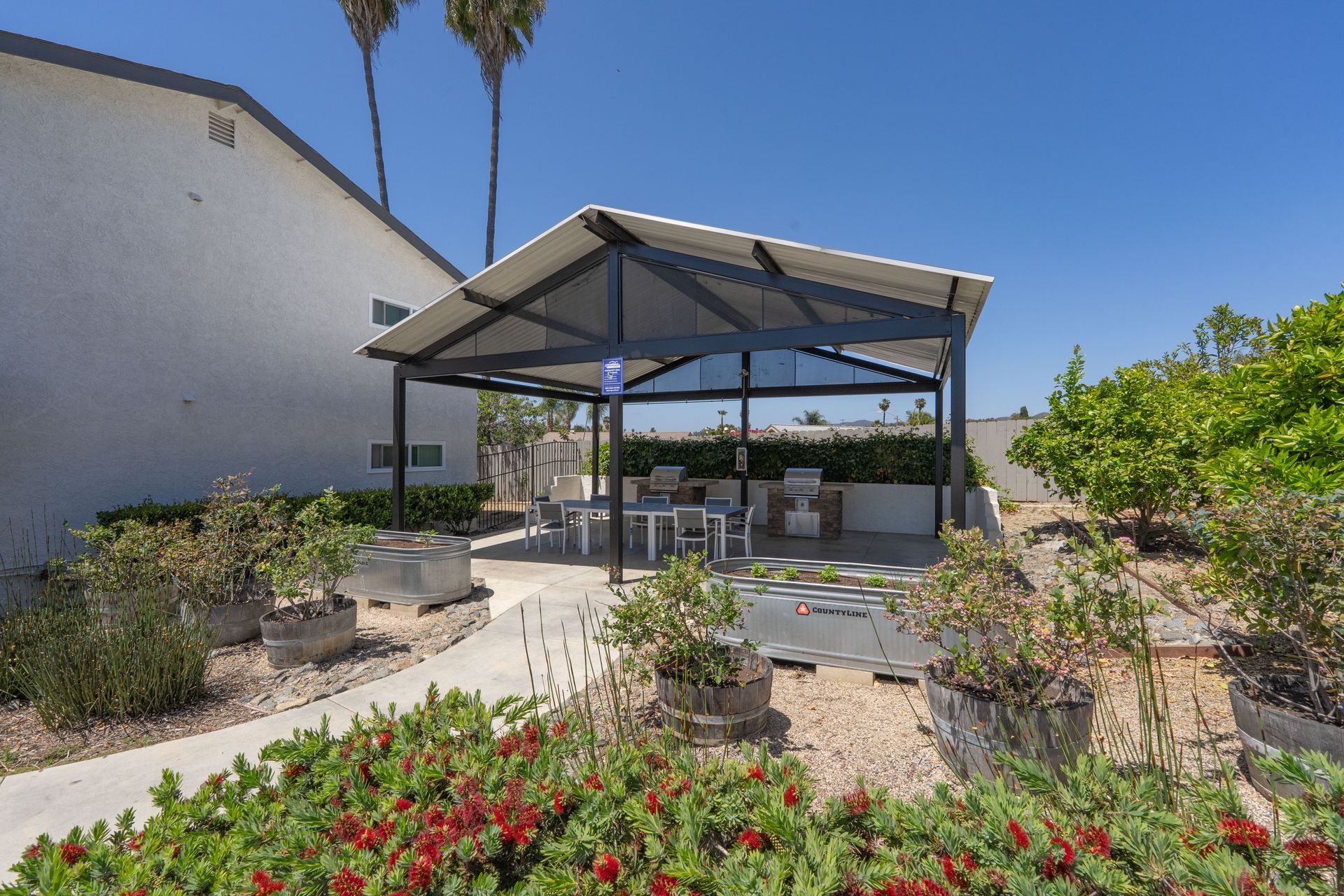 Outdoor patio with a gazebo, landscaped plants, and benches under a blue sky