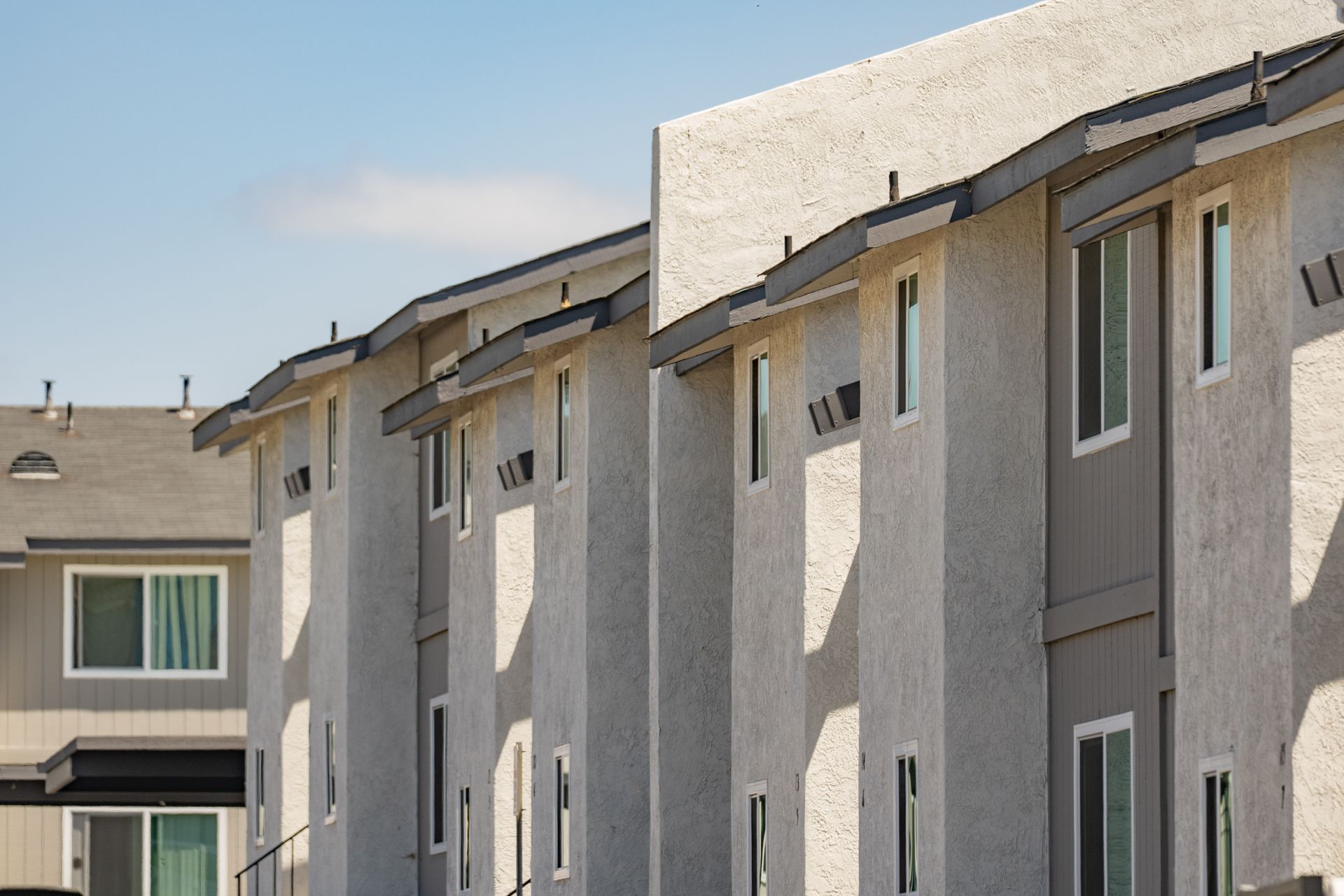 Row of beige apartment buildings with white-trimmed windows under a clear blue sky