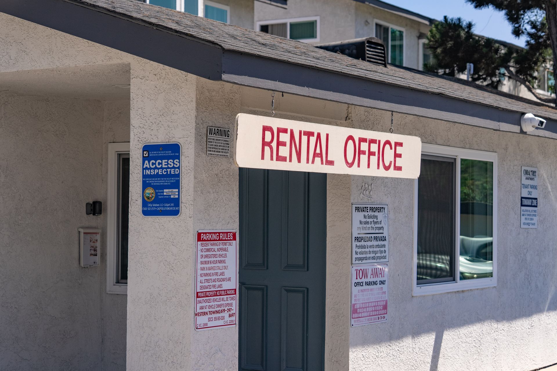 Rental office entrance with white stucco wall, gray door, and red sign above the doorway.