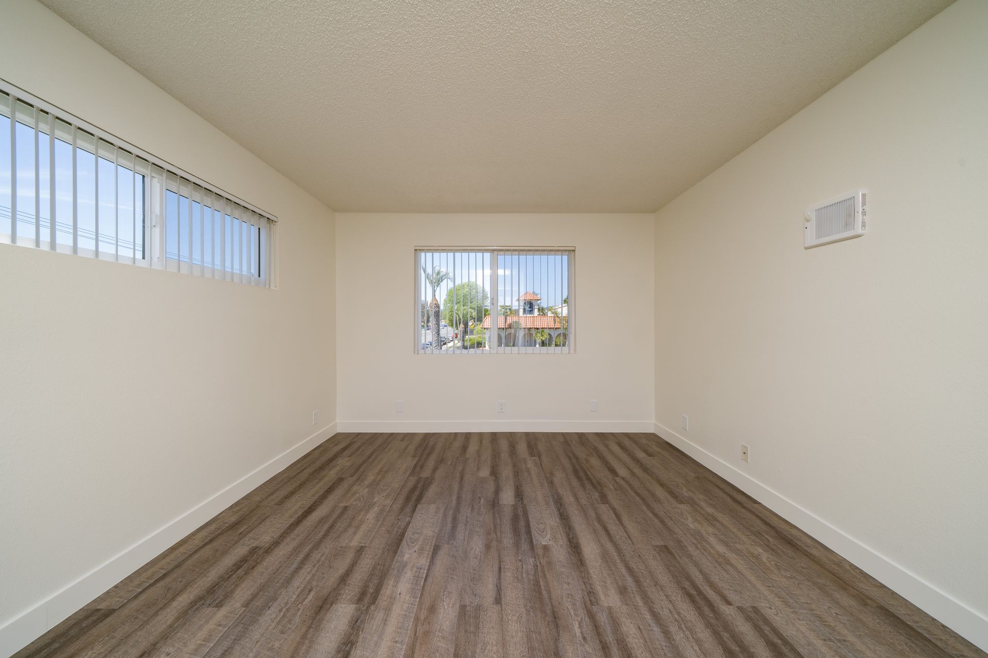 Empty room with white walls, wood-look flooring, and two windows letting in natural light