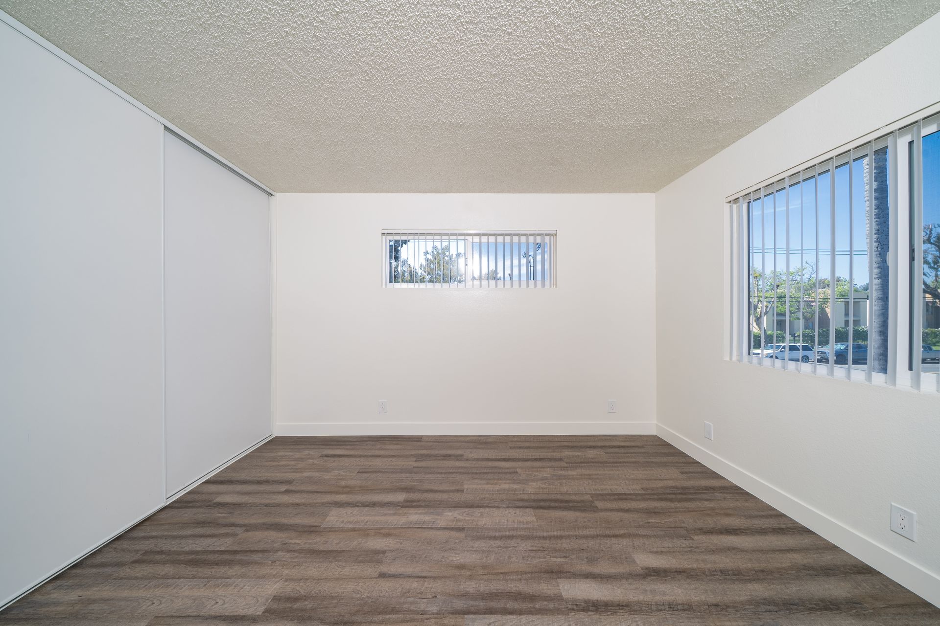 Empty beige room with wood flooring and a small window on the far wall.