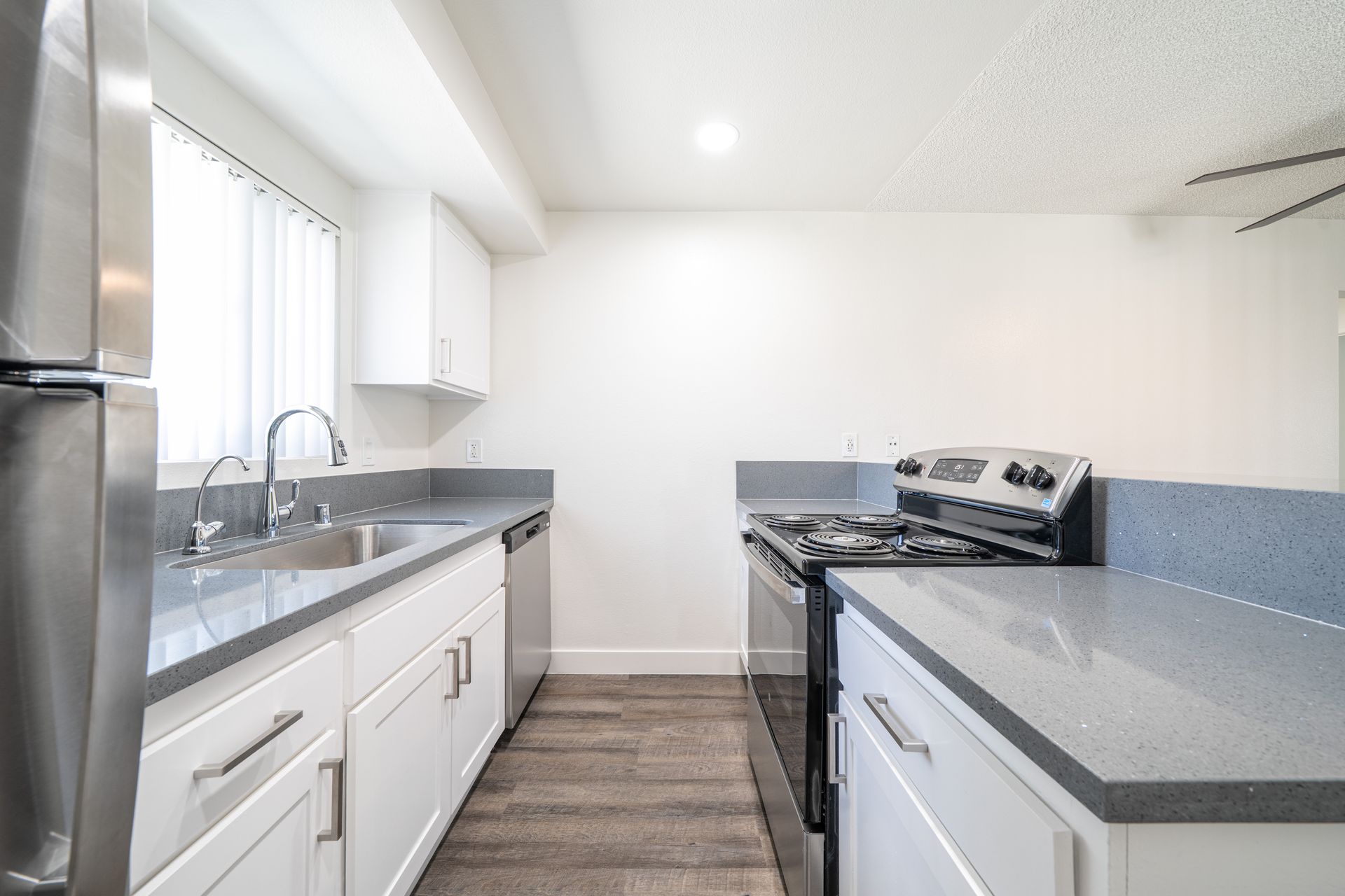 Bright modern kitchen with white cabinets, gray countertops, and a stainless steel stove and sink.
